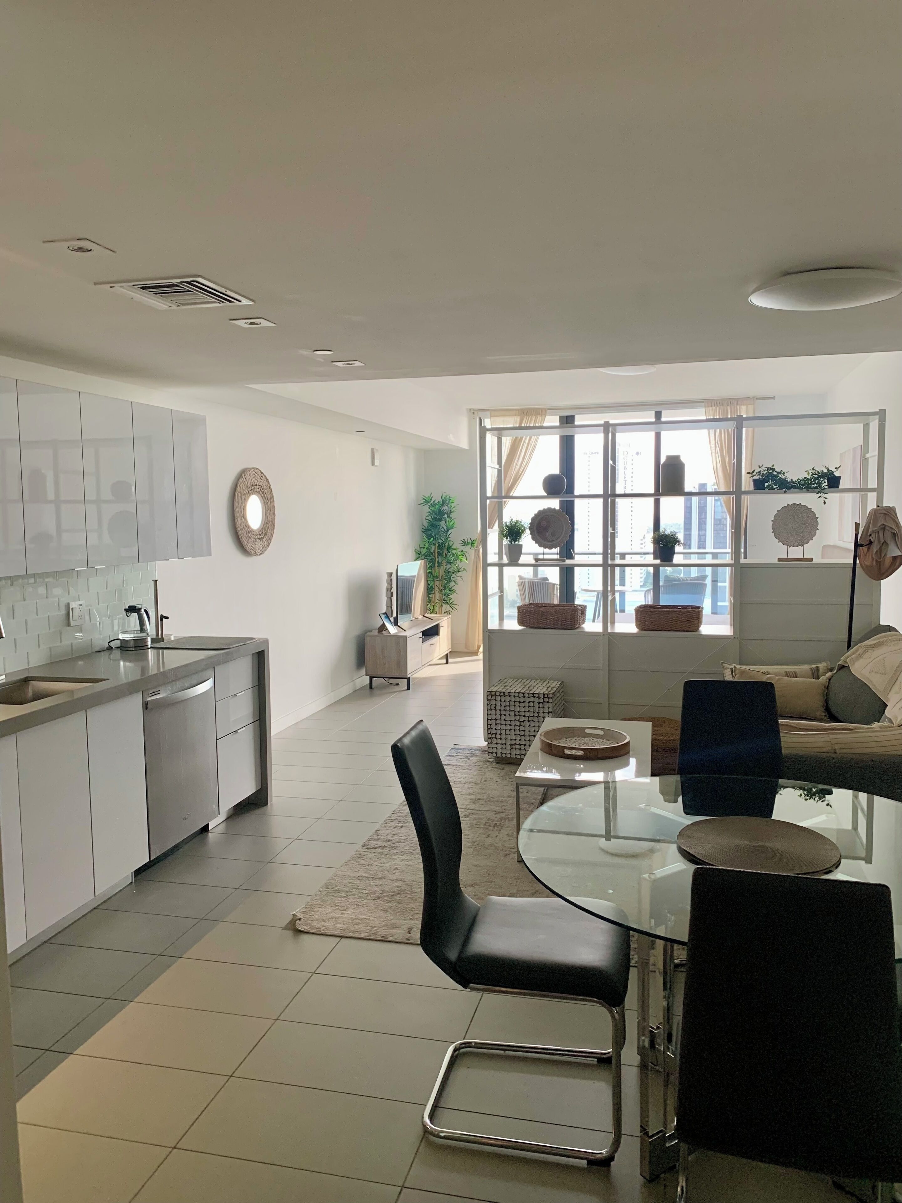 A modern kitchen with a central island, a dining area with a glass table and chairs, and a seating area with a sofa and a coffee table.