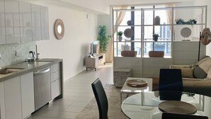 A modern kitchen with a central island, a dining area with a glass table and chairs, and a seating area with a sofa and a coffee table.