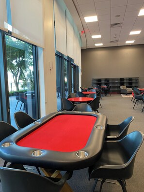 A billiards table with chairs, a red tablecloth, and a view of the outdoors through large windows.