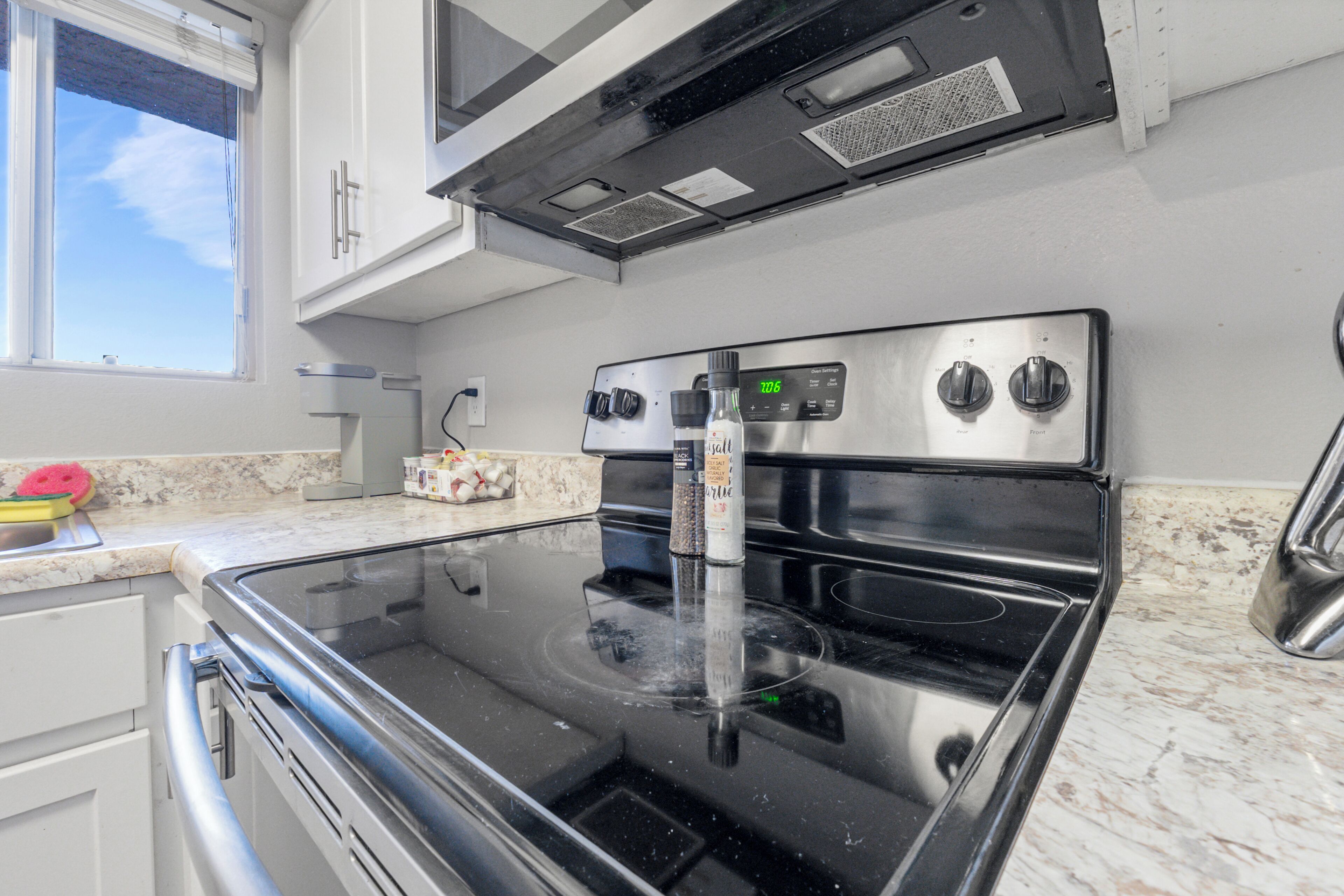 A kitchen with a stainless steel stove, a window, and a marble countertop.