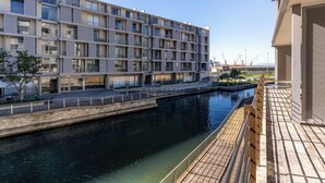 Ein modernes, mehrgeschossiges Gebäude mit Balkonen, einem Kanal und einer Fußgängerbrücke.