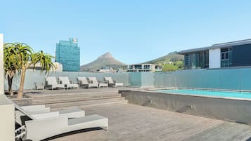 A rooftop pool area with lounge chairs, a pool, and a view of a mountain and a building.