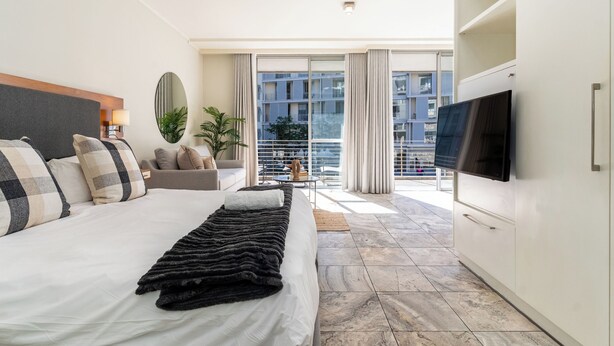 Ein modernes Hotelzimmer mit einem großen Bett, einem Flachbildfernseher, einem Balkon mit Blick auf die Stadt und einem Sofa.