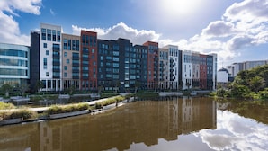 A modern hotel with multiple floors, a reflective water body in front, and a clear sky. - Cosy and Charming Bridgewater One Apartment | Wifi (Cape Town)