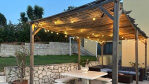 A covered outdoor patio with stone walls, a stone staircase, and a seating area with cushions.