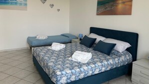 A bedroom with a large bed, two smaller beds, a nightstand, and a wall with heart-shaped decorations and a sunset painting.