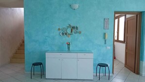 A room with a blue wall, a white cabinet, two black stools, and a small table with a vase of flowers.