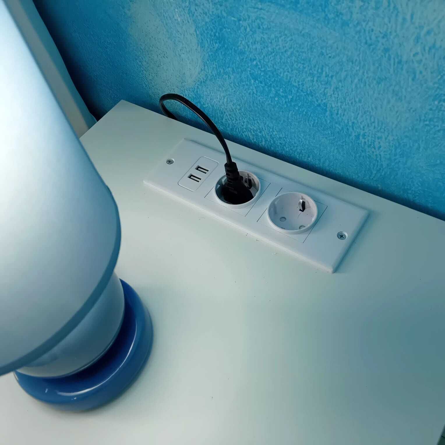 Une table blanche avec une prise électrique, une lampe et un mur bleu.