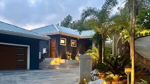 Una casa moderna con garaje, un acceso bien iluminado y un jardín ajardinado con rocas y plantas.