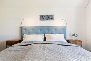 Ein Bett mit gestepptem Kopfteil, zwei Kissen und ein Nachttischchen mit einer Lampe.