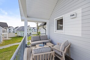 Eine überdachte Veranda mit einer Couch und Sesseln, einem kleinen Tisch und einem Fenster mit der Nummer 116b.