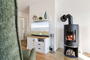 A modern living room with a black wood-burning stove, a flat-screen TV mounted on a white cabinet, and a small shelf with decorative items.