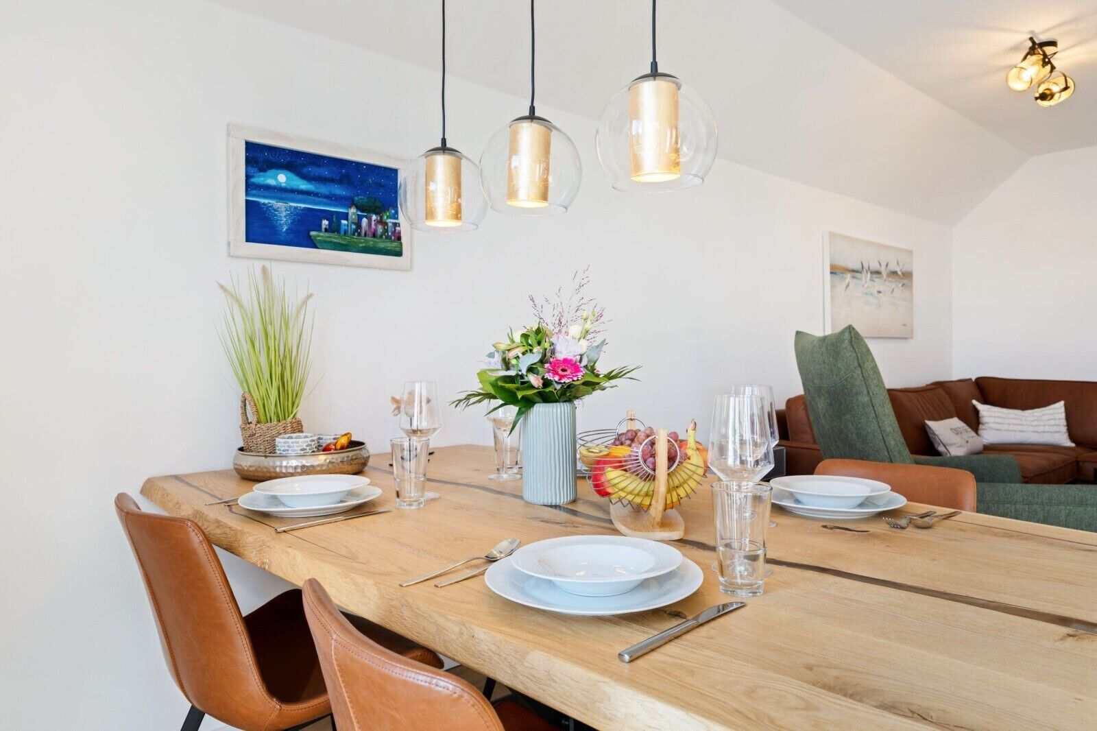 A dining area with a wooden table set for four, clear glassware, and a vase with flowers.