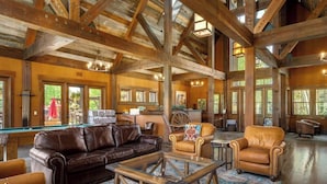 A spacious room with a pool table, leather sofas, and a rustic wooden ceiling.