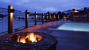 A pool area with a fire pit, wooden cabins, and a metal fence.