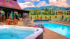 A pool area with a hot tub, lounge chairs, and a view of mountains.