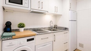 Une cuisine compacte équipée d’un four à micro-ondes, d’un évier, d’un lave-linge et d’une petite plante en pot.