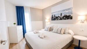 Une chambre d’hôtel moderne, dotée d’un grand lit, de tables de chevet, d’une commode et offrant une vue sur l’océan.