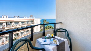Un balcon avec une table dressée pour deux personnes, offrant une vue sur la côte et sur les bâtiments qui se dessinent à l’arrière-plan.