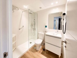 A modern bathroom with a glass shower enclosure, a white toilet, a sink with a mirror, and a hairdryer mounted on the wall.