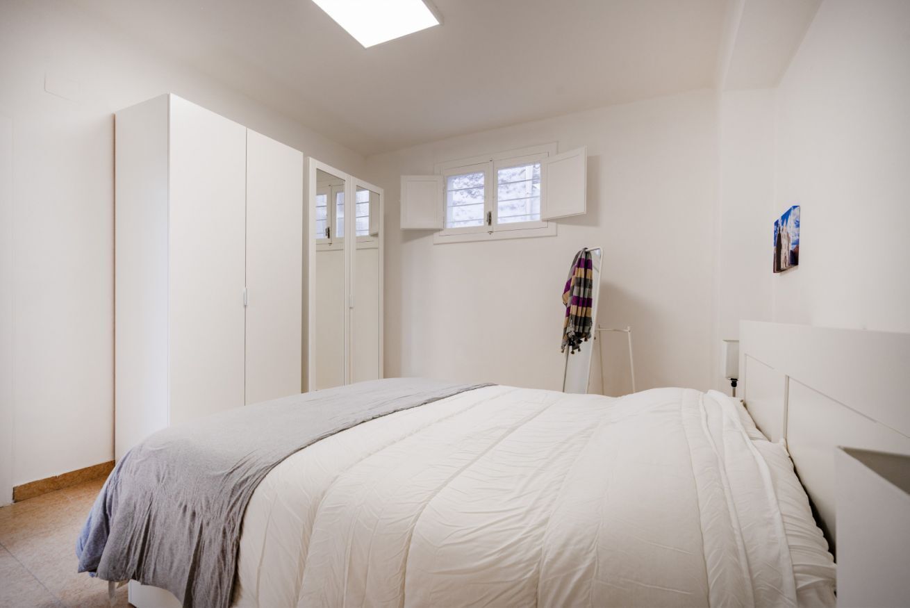 Ein Schlafzimmer mit einem Bett, einem Kleiderschrank, einem Fenster und einem an der Wand hängenden Kunstwerk.