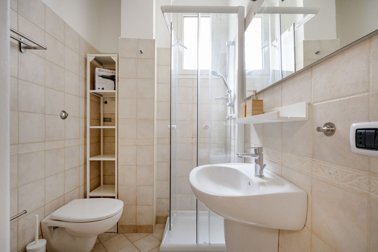 A bathroom with a toilet, a glass shower enclosure, a sink, and a mirror.