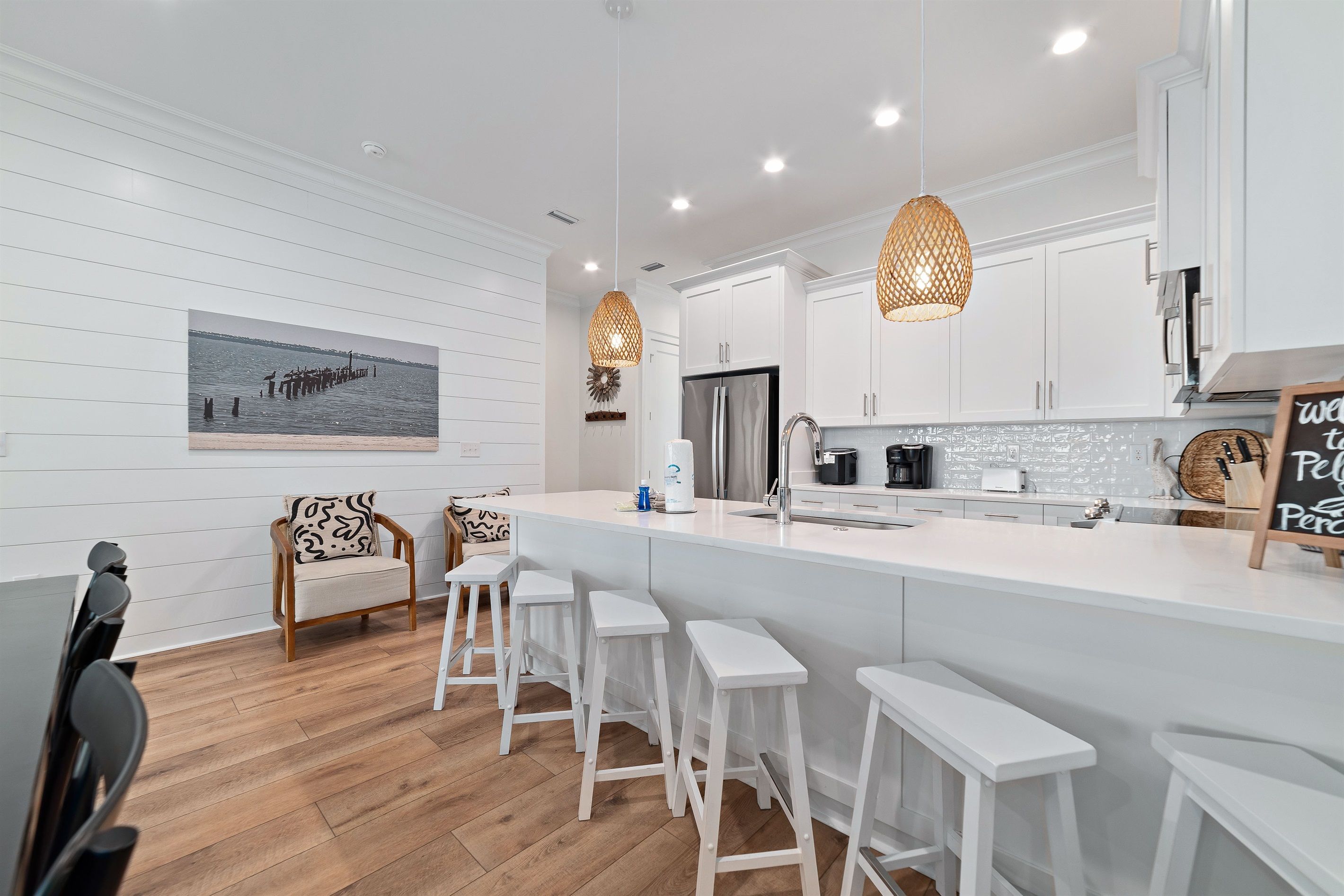 A modern kitchen with white cabinetry, a large island with bar stools, pendant lighting, and a view of the water.