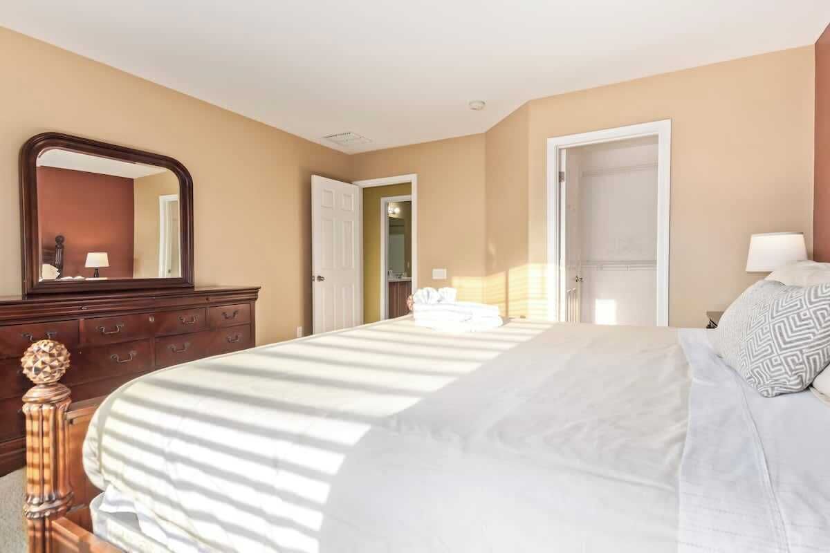 Una habitación de hotel con una cama grande, un aparador, un espejo y una puerta que da a otra habitación.