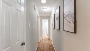 Un couloir doté d’un plancher en bois, de murs blancs et d’œuvres d’art encadrées.