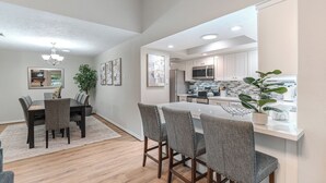Une cuisine moderne avec des meubles blancs, un îlot central et un coin repas comprenant une table et des chaises.
