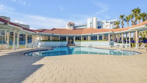 Ein Schwimmbecken mit gefliestem Sonnendeck, einem überdachten Sitzbereich und Palmen im Hintergrund.