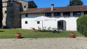A white building with a tiled roof, a stone tower, and a patio with outdoor furniture. - Foresteria Casaforte Bergum at the gates of Cividale (Friuli-Venezia Giulia)