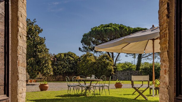 An outdoor patio area with a stone archway, a table with chairs, and a large umbrella providing shade. - Foresteria Casaforte Bergum at the gates of Cividale (Friuli-Venezia Giulia)