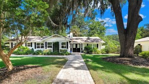 A single-story house with a brick pathway leading to the front door, surrounded by lush greenery and trees. - Gator Shack, Luxury Chic! (Gainesville)