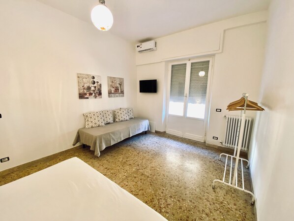 A room with a bed, a bench, a radiator, and a wall-mounted TV.
