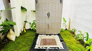 Un petit jardin clos, avec un mur en briques, un élément décoratif aquatique et une variété de plantes.