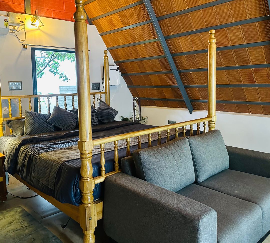 Un lit à baldaquin avec un cadre en bois et un canapé gris dans une pièce dont le plafond est en pente.