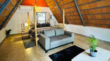 Une chambre mansardée chaleureuse avec un plafond en pente, un lit à baldaquin, un canapé gris, une petite table et une plante en pot.