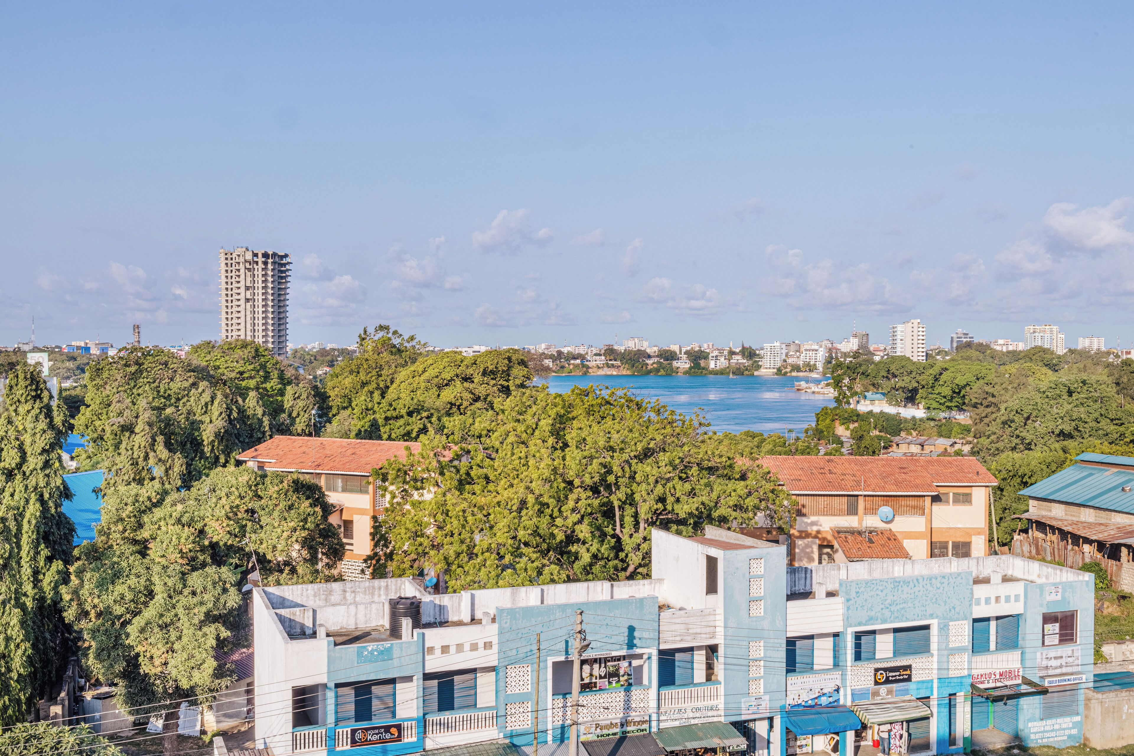Un paysage urbain côtier, avec un mélange de bâtiments résidentiels et commerciaux, un gratte-ciel imposant et une vue sur la mer.