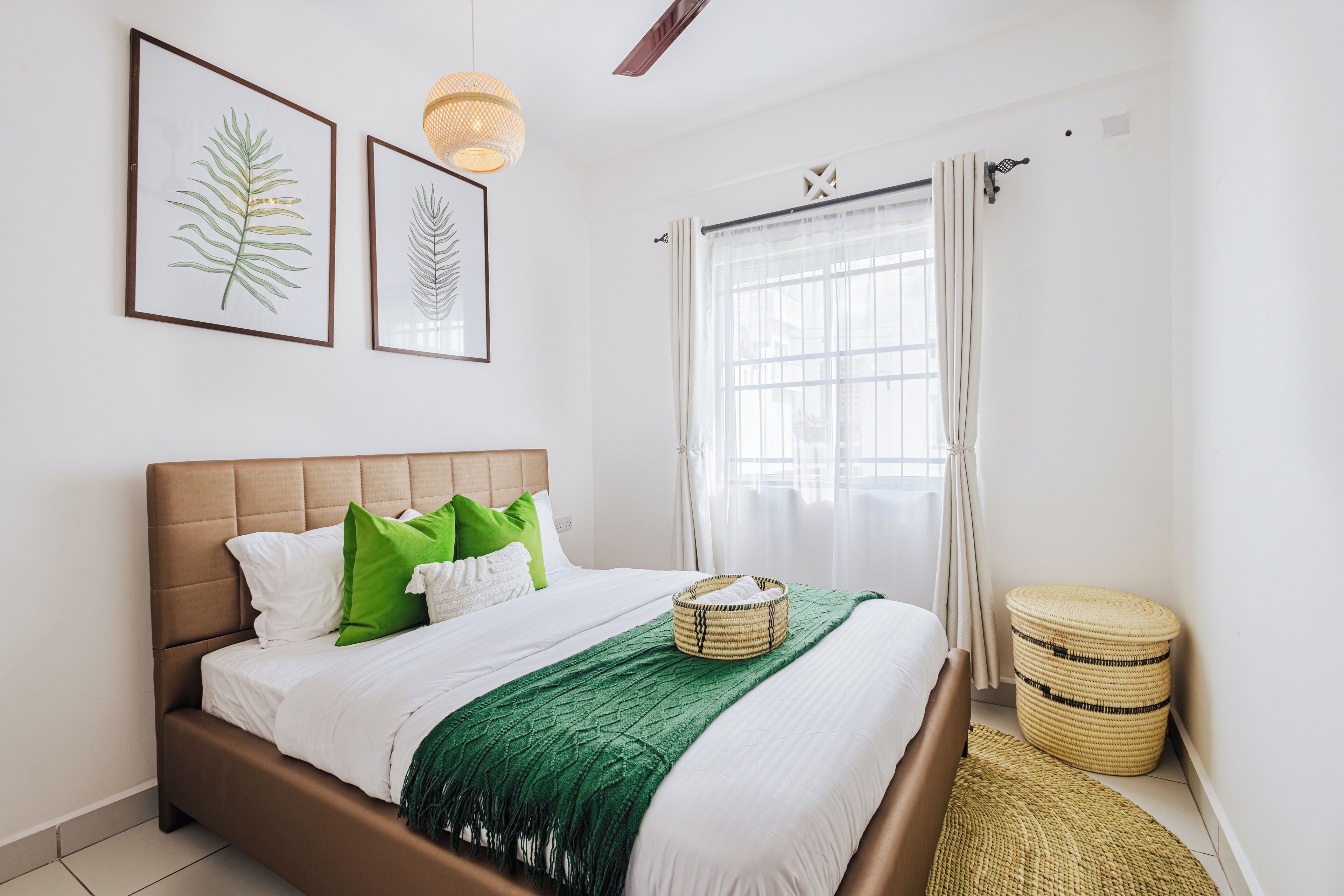 Una cama bien hecha con ropa de cama verde y blanca, una cesta tejida sobre la cama y un taburete tejido a un lado.