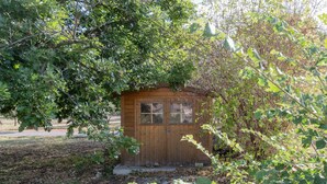 A small wooden shed with a door and windows, surrounded by dense foliage. - Holiday Home 'Chêne' with Mountain View, Wi-Fi and Air Conditioning (Les Vans)