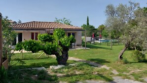 A house with a tiled roof, a garden with a large tree, and a pool in the background. - Holiday Home 'Chêne' with Mountain View, Wi-Fi and Air Conditioning (Les Vans)