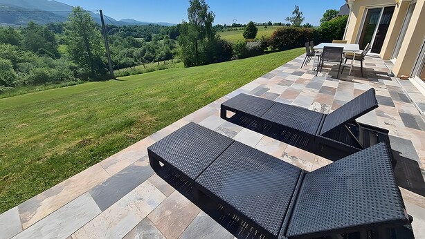 Une terrasse avec deux fauteuils de relaxation noirs, une table et une vue sur un paysage verdoyant, avec des arbres et des collines.