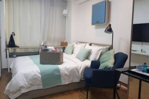 Habitación de hotel con cama, una silla, un escritorio, televisor y ventana con cortinas.