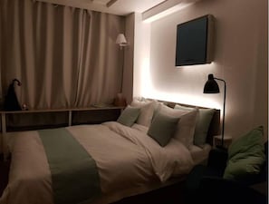 Une chambre d’hôtel avec un lit, des lampes de chevet, un téléviseur fixé au mur et une fenêtre avec des rideaux.