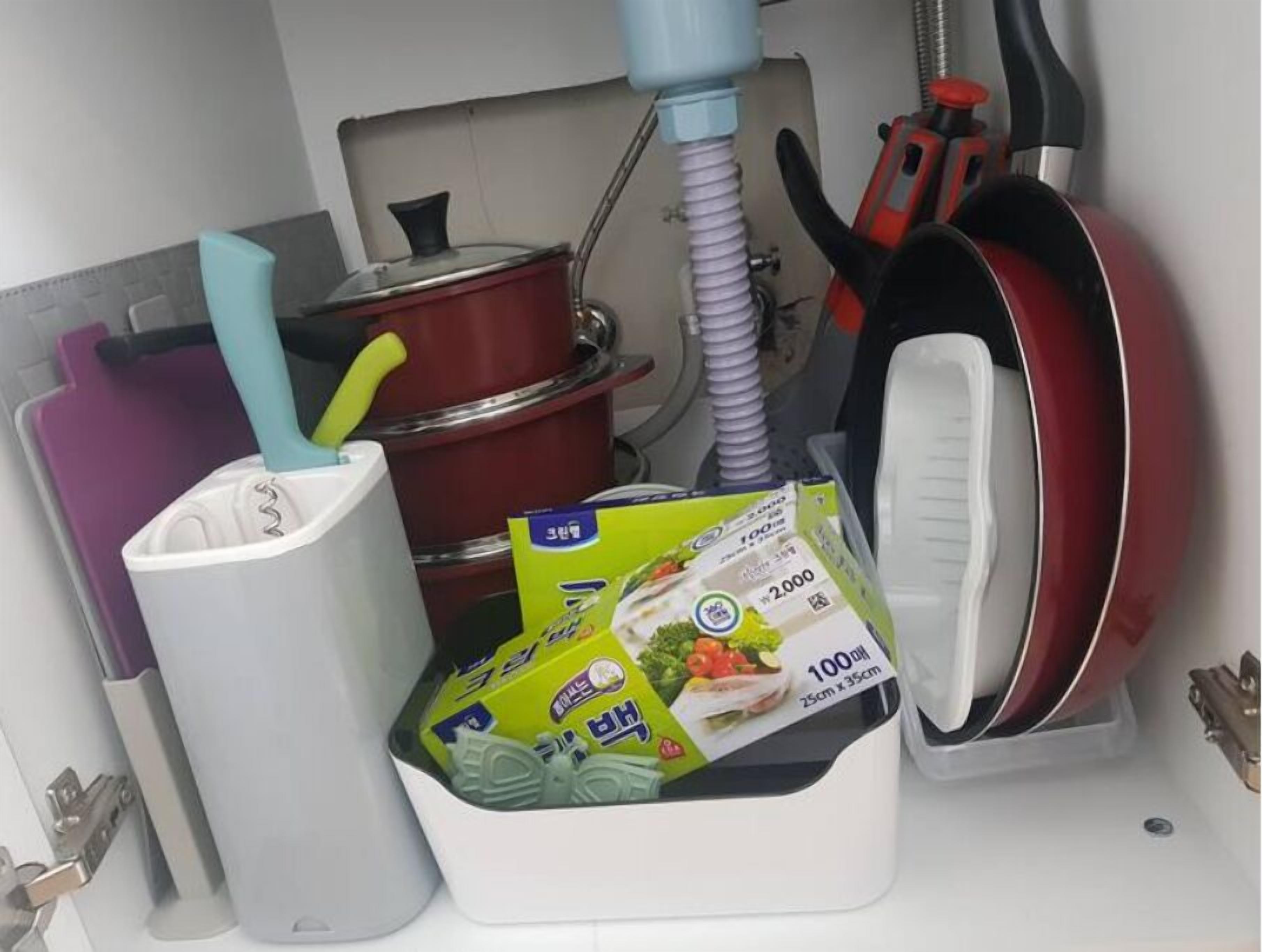 A kitchen with a white sink, a red pot, a green package of food, and a red pan.