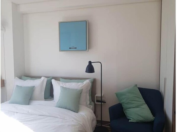 Habitación de hotel con cama, escritorio, silla, lámpara y un cuadro en la pared.