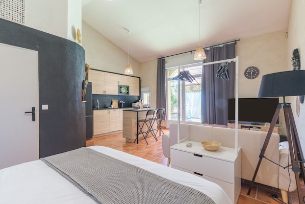 A modern hotel room with a bed, a small desk, a chair, a TV, and a tripod.