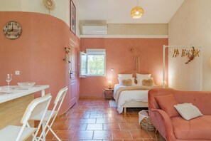 Ein Zimmer mit einem Bett, einer Couch, einem Esstisch mit Stühlen, einem Fenster und einer Wanduhr.