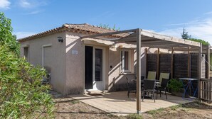 Un petit bâtiment doté d’un toit en tuiles, d’un patio couvert avec des meubles d’extérieur et d’une clôture en bois.